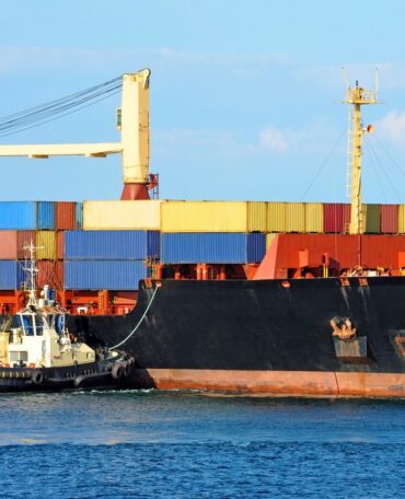 Tugboat assisting container cargo ship to harbor quayside
