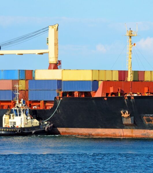 Tugboat assisting container cargo ship to harbor quayside