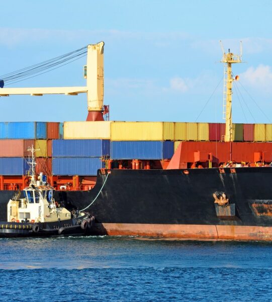 Tugboat assisting container cargo ship to harbor quayside