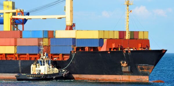 Tugboat assisting container cargo ship to harbor quayside