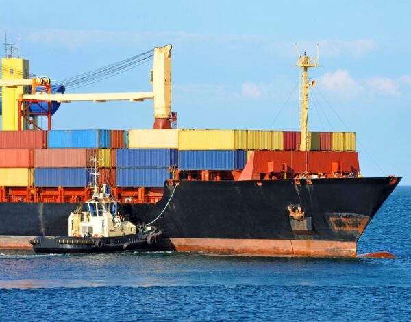 Tugboat assisting container cargo ship to harbor quayside
